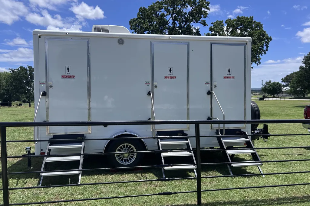 Side view of a three-door luxury restroom trailer with fold-out steps at a Tarrant County property